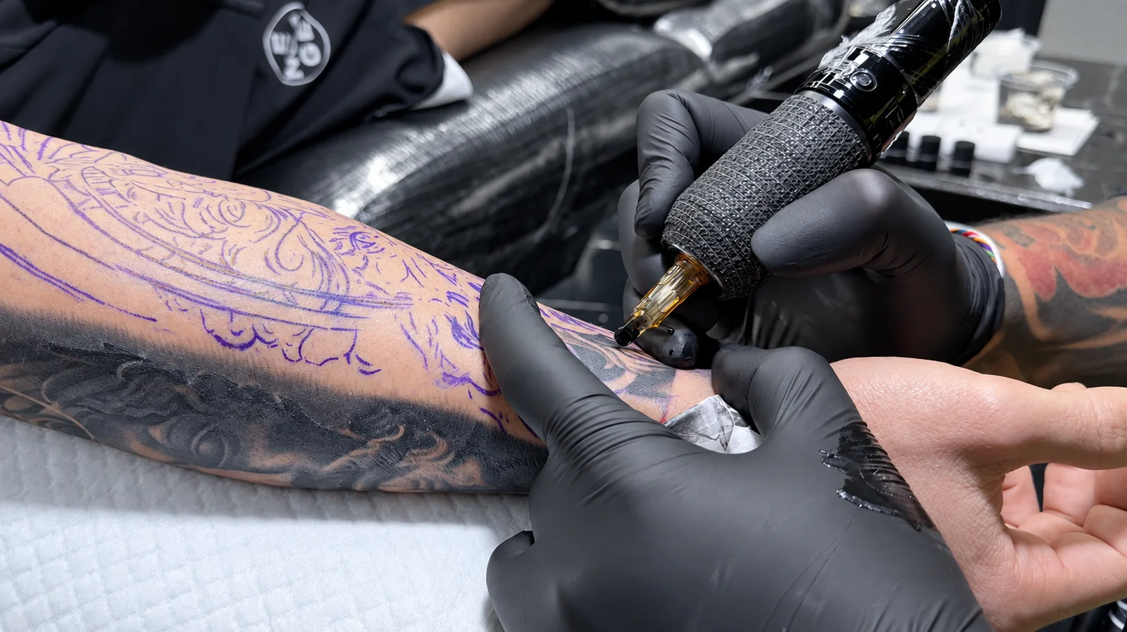 Close-up of a gloved tattoo artist working on a customer's forearm with a tattoo machine
